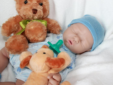 A baby doll wearing a blue hat is resting on a soft white blanket.